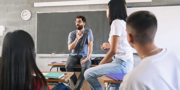 Innostunut miesopettaja puhuu ja oppilaat kuuntelevat kiinnostuneina.