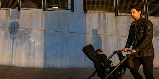 Isä työntämässä rattaissa pientä lasta. Taustalla betoninen seinä.