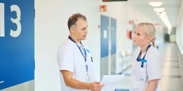 Keusote aloittaa uudet yt-neuvottelut. Kaksi hoitajaa keskustelemassa sairaalan käytävällä.