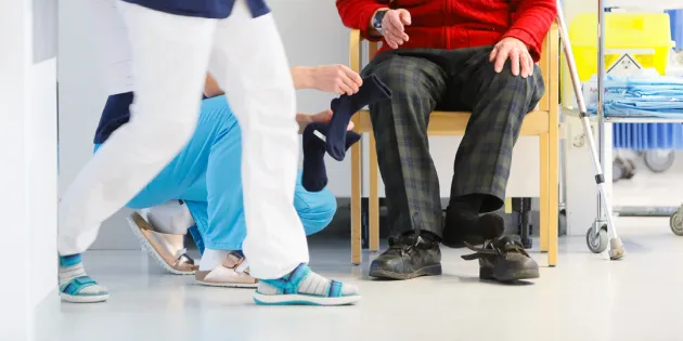 Kiireisiä hoitajia sairaalan käytävällä. Vanhus istuu tuolissa.