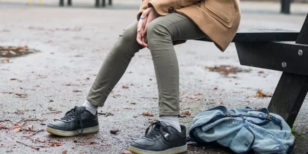 Lasten ja nuorten keskinäinen kiusaaminen rakentuu vähitellen. Yksinäinen lapsi koulun pihalla. Reppu maassa ja syksyisiä lehtiä asfaltin pinnalla.