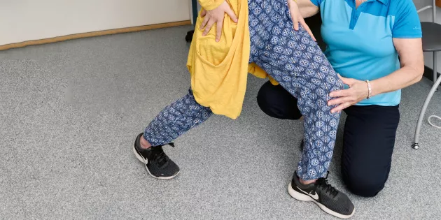Kuntoutuksen ammattilainen ohjaa asiakasta jalasta kiinni pitäen.