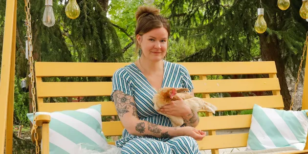 Julia Lehtilä istuu keltaisessa pihakeinussa kana sylissään.