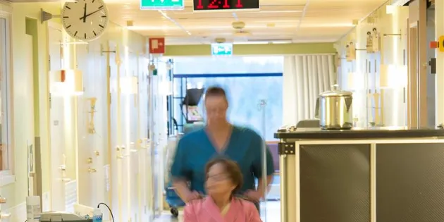 Hoitaja työntää potilasta pyörätuolissa laitoksen käytävällä.