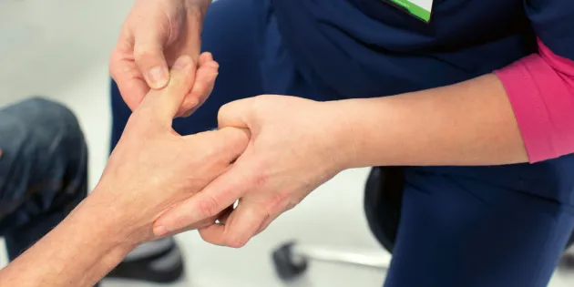 Fysioterapeutti tutkii potilaan kättä. 