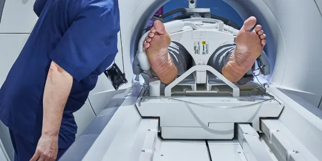 Potilas menossa magneettikuvaukseen koneeseen. Hoitaja varmistamassa vierellä.