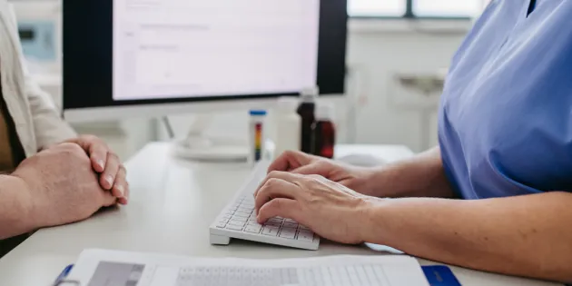 Hoitaja keskustelee potilaan kanssa. Taustalla tietokoneen näyttö.