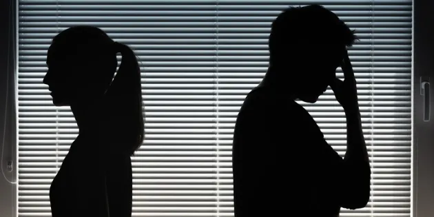 Miehen ja naisen tummat varjosiluetit sälekaihtimilla peitettyä ikkunaa vasten selin toisiinsa.