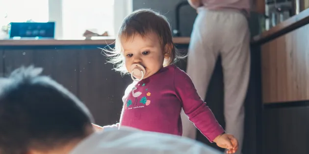 Pieni lapsi kodin keittiössä isoveljen kanssa. Taustalla vanhempi tiskaamassa.