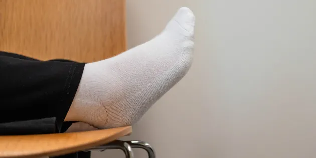 Jalka lepäämässä tuolin päällä. Näkyy vain hiukan lahjetta ja valkoinen sukka.