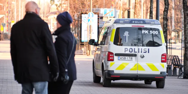 Poliisiauto katukiveyksellä. Vieressä muutama ihmishahmo selin kameraan päin.