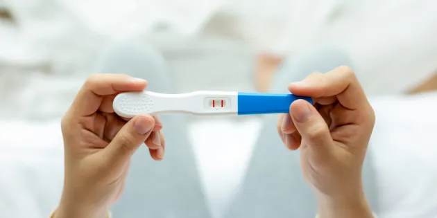 Henkilö pitää kädessään positiivista raskaustestiä.