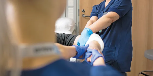 Kaksi hoitajaa käsittelee potilaan kipsattua kättä. 