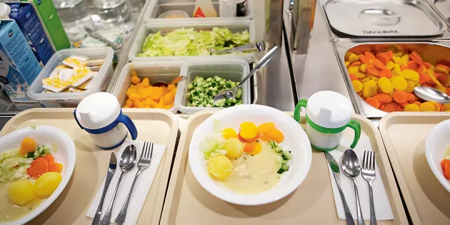 Päiväkodin ruokalinjastolla tarjottimilla annoksia valmiina. Lautasella perunoita ja vihanneksia.