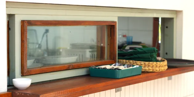 Kuva ruokalinjaston luukku ja pieni ikkuna, josta näkee läpi keittiöön.