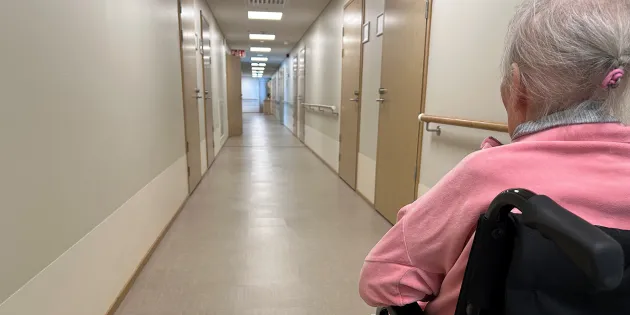 Palvelutalon pitkä käytävä ja vanhus pyörätuolissa.