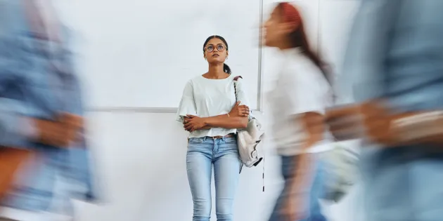 Nainen seisoo kiirehtävien ihmisten keskellä stressaantuneena kädet puuskassa ja katsoo ylöspäin.