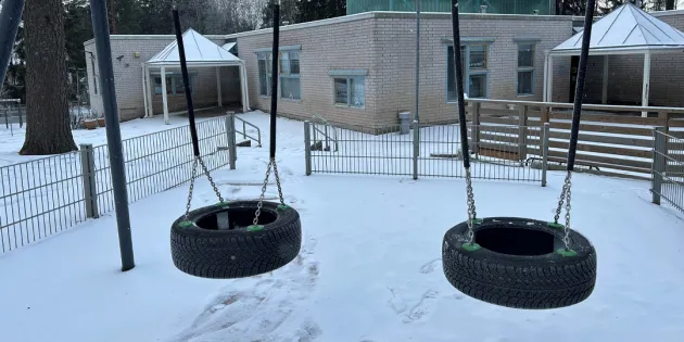 Talvinen kuva tyhjästä päiväkodin pihasta, jossa kaksi rengaskeinua.