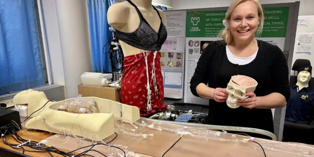 Yliopistotutkija Mariella Särestöniemi Human Body Twin -laboratoriossa, jossa kehitetään teknologiaa, joka mahdollistaa terveydentilan seurannan ja arvioinnin kannettavilla ja päälle puettavilla mittalaitteilla. Kädessään hänellä on aivomalli, jota käytetään signaalin etenemisen tutkimiseen aivokudoksessa, ja taustalla nukella on rintasyövän tunnistukseen kehitettävät monitorointiliivit. 