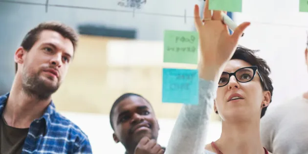 Työtiimi tekee suunnittelutyötä yhdessä kiinnittäen post it -lappuja lasiseinälle.