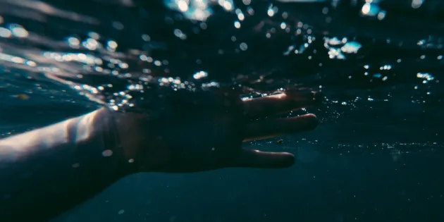 Ihmisen käsi veden pinnan alapuolella. Vesi on synkkää ja tummaa. Vedestä pelastettu potilas puri ja uhkasi tappaa ensihoitajat.