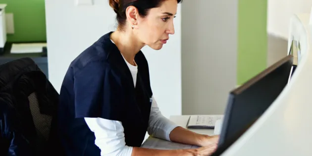 Hoitaja klinikan tietokoneella katsoo vakavana näyttöä.
