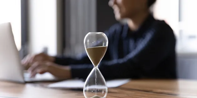 Ihminen läppärillä, etualalla tiimalasi.