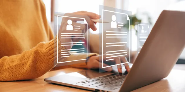 Henkilö käyttää kannettavaa tietokonetta pöydän ääressä ja selaa virtuaalisia tiedostoja, jotka näkyvät läpinäkyvinä kuvakkeina näytön edessä.