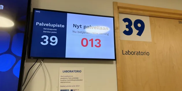 Työterveyshuolto maksoi noin 600 euroa työntekijää kohti. Yksityisen lääkäriaseman odotustila ja vuoronumerot television näytöllä.