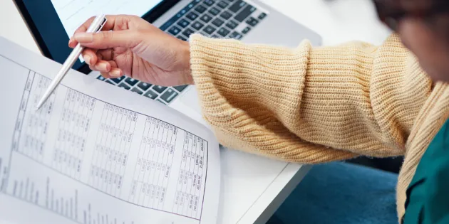 Nainen tarkastelee paperisia tositteita. Ansiopäivärahan porrastus näkyy, kun työttömyys pitkittyy.