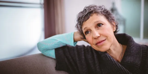 Hieman hiuksista harmaantunut nainen nojaa käteensä ja katsoo ikkunasta ulos.