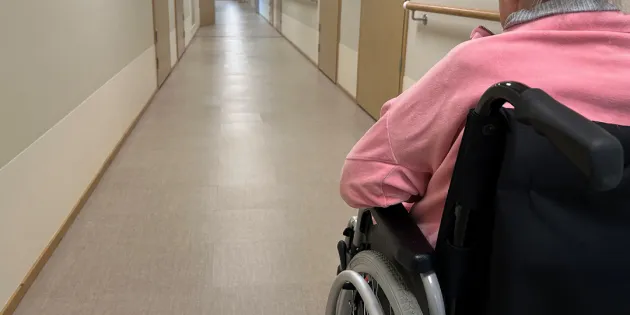 Vanhus sairaalan käytävällä pyörätuolissa. Puutteellinen kielitaito kuormittaa vanhusten hoidon työyhteisöjä ja vaarantaa potilasturvallisuutta.