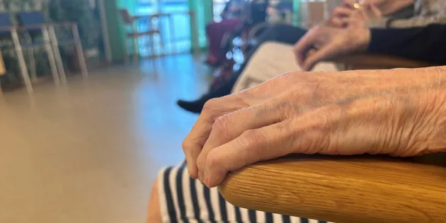 Vanhus lepuuttaa kättään tuolin käsinojalla. Lähikuva ryppyisestä kädestä.