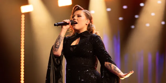 Tampereella työskentelevä sairaanhoitaja Justiina Luukaslammi on edennyt The Voice of Finlandissa semifinaalivaiheeseen. Justiina laulaa mikrofoniin tummassa dramaattisessa mekossa.