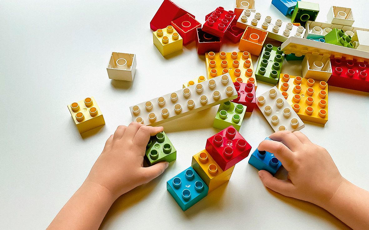 Lapsen kädet rakentavat tornia Lego-palikoista.