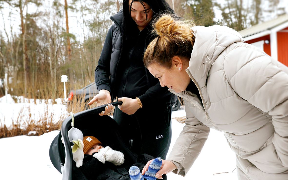 Tanja Nyström on kumartuneena katsomaan lapsenlastaan Papusta. Vieressä on tytär Erica.