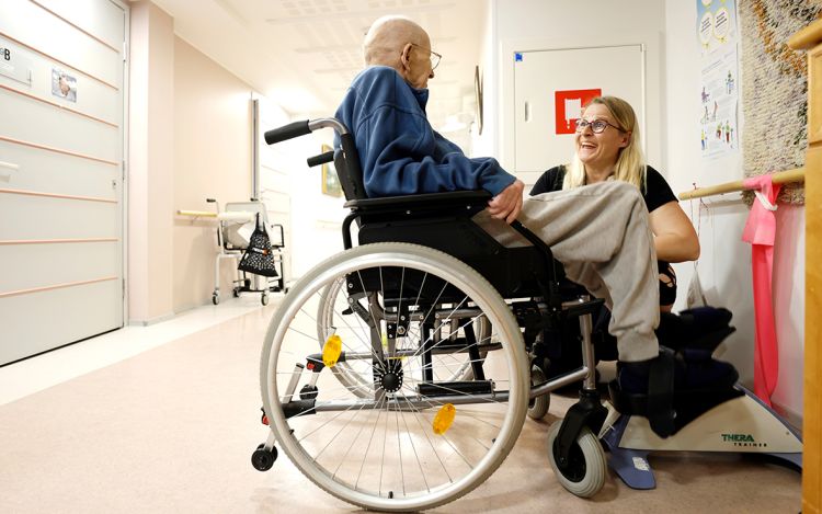 Lähihoitaja Kirsi Lindeqvist on kumartunut pyörätuolissa olevan vanhuksen puoleen.