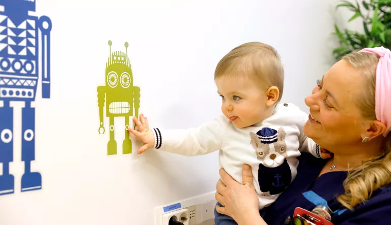 Vauva tutkii robotin kuvaa seinällä.