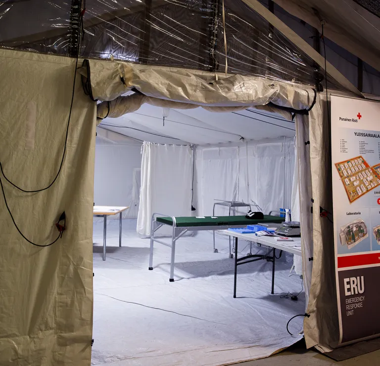 Kenttäsairaalan teltta kuvattu ulkoa niin että sisällä olevat välineet näkyvät auki jätetystä aukosta.