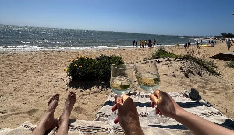 Rantanäkymä. Kuvassa näkyy kaksi kättä, joissa viinilasit.