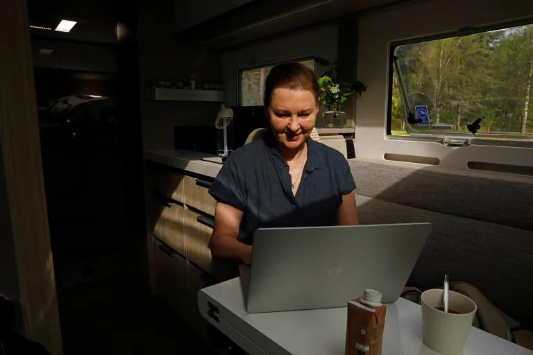 Eija laine kirjoittamassa läppärillä matkailuauton pöydän ääressä.