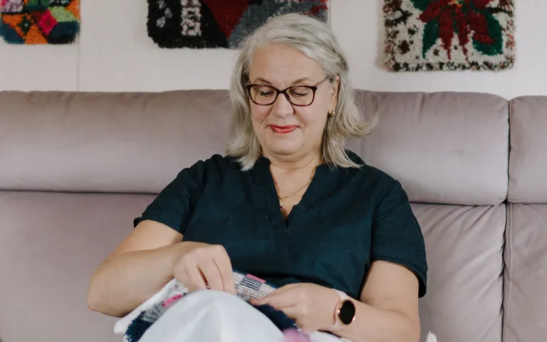 Marja-Liisa Haapakorva viimeistelee ryijyä olohuoneensa sohvalla.