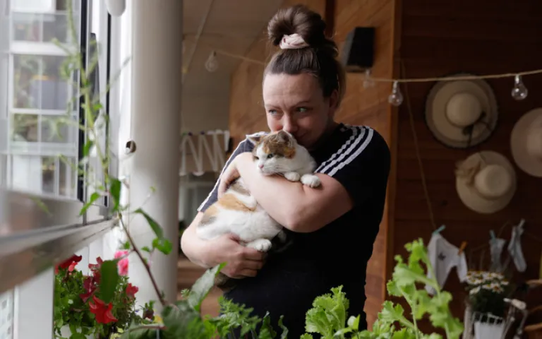 Lähihoitaja Kiia Malin Miiru-kissa sylissään Kontulan seniorikeskuksen parvekkeella.
