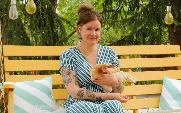 Julia Lehtilä istuu keltaisessa pihakeinussa kana sylissään.