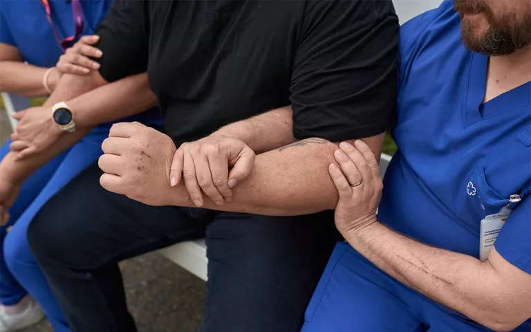 Kaksi hoitajaa pitää potilasta kiinni käsivarsista.