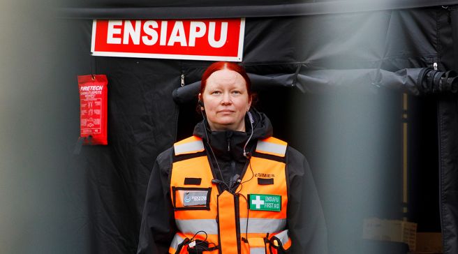 Terhi Kiikala seisoo ensiaputeltan edessä, päällään oranssi liivi.