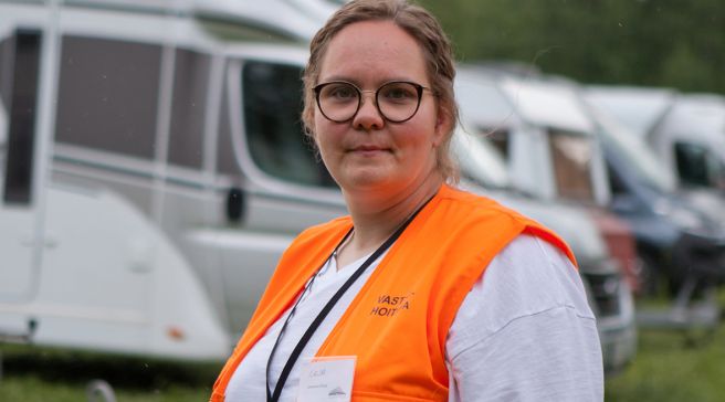 Erja Koskela seisoo matkailuvaunurivistön edessä päällään oranssi liivi.