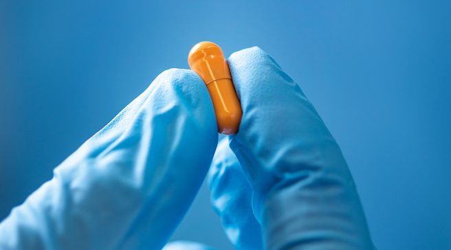 Oranssi lääke etusormen ja peukalon välissä.