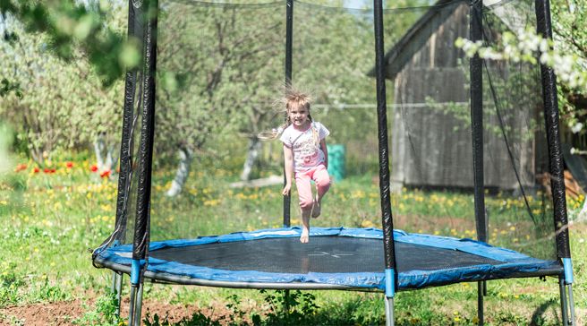 Pieni tyttö hyppii trampoliinilla, jossa on oikeaoppinen turvaverkko ja pehmusteet.