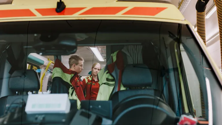 Ensihoitajaopiskelija Veeti Soini ja ensihoitaja Essi Lilja seisomassa ambulanssin takana.